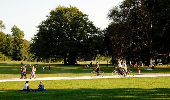 A park with many people riding bikes, having a picnic, and walking.